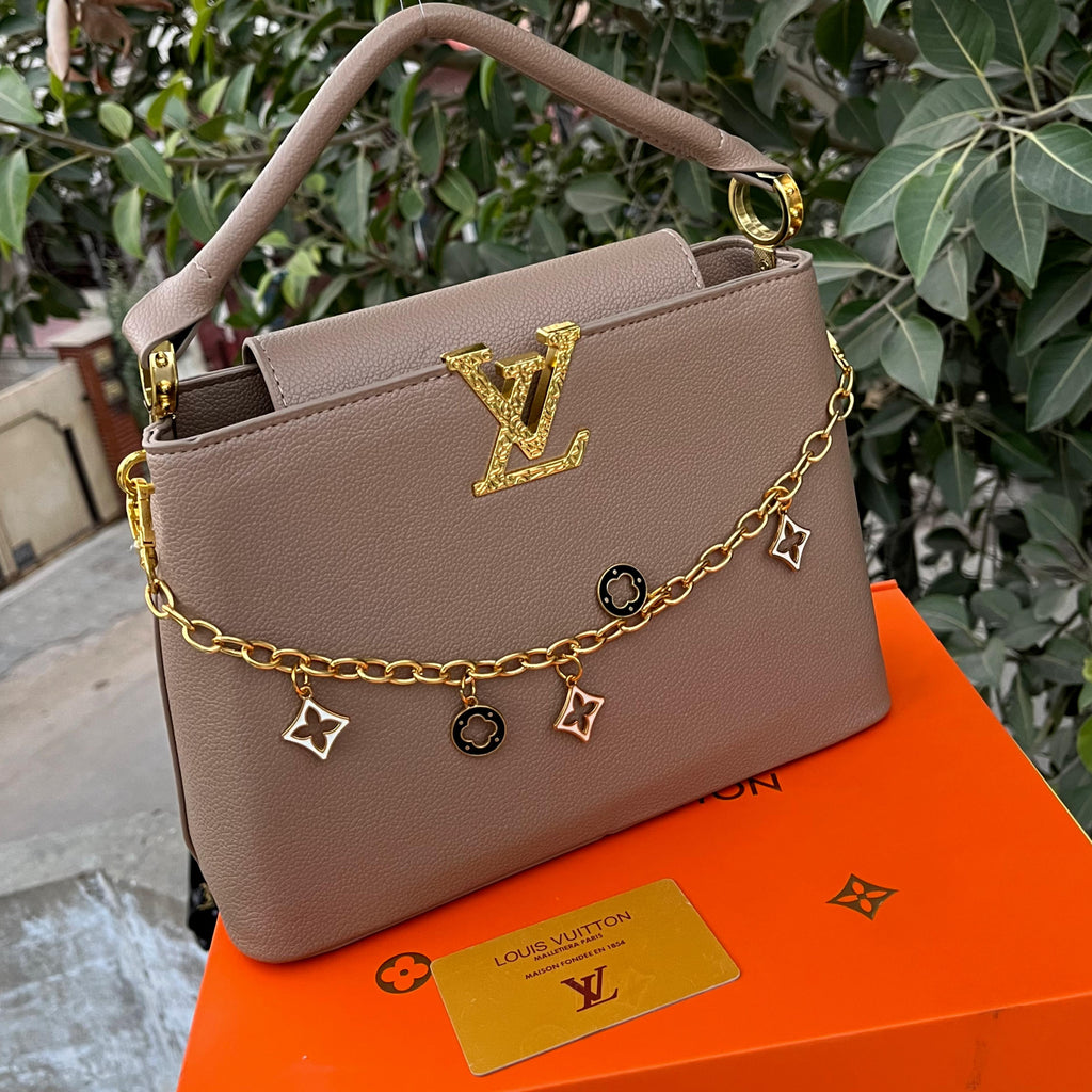 Louis Vuitton handbag with gold chain and charms on an orange box with brand card, outdoor setting.