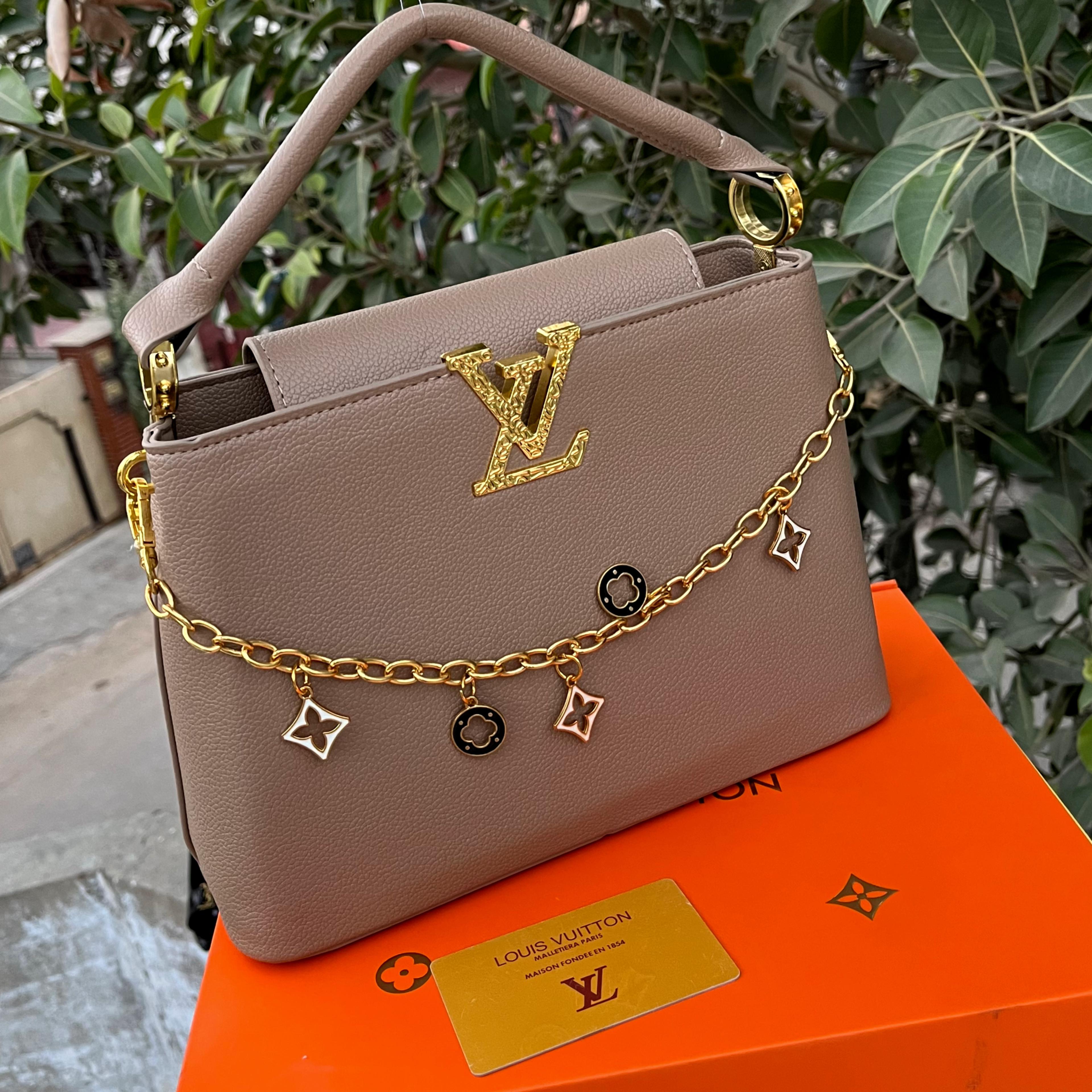 Louis Vuitton handbag with gold chain and charms on an orange box with brand card, outdoor setting.